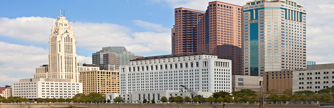 Skyline view of several high-rise buildings on a sunny day with a partly cloudy sky, featuring diverse architectural styles.