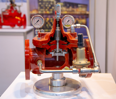 Cutaway model of an industrial valve showing internal components, including gauges and pipes on a display stand.